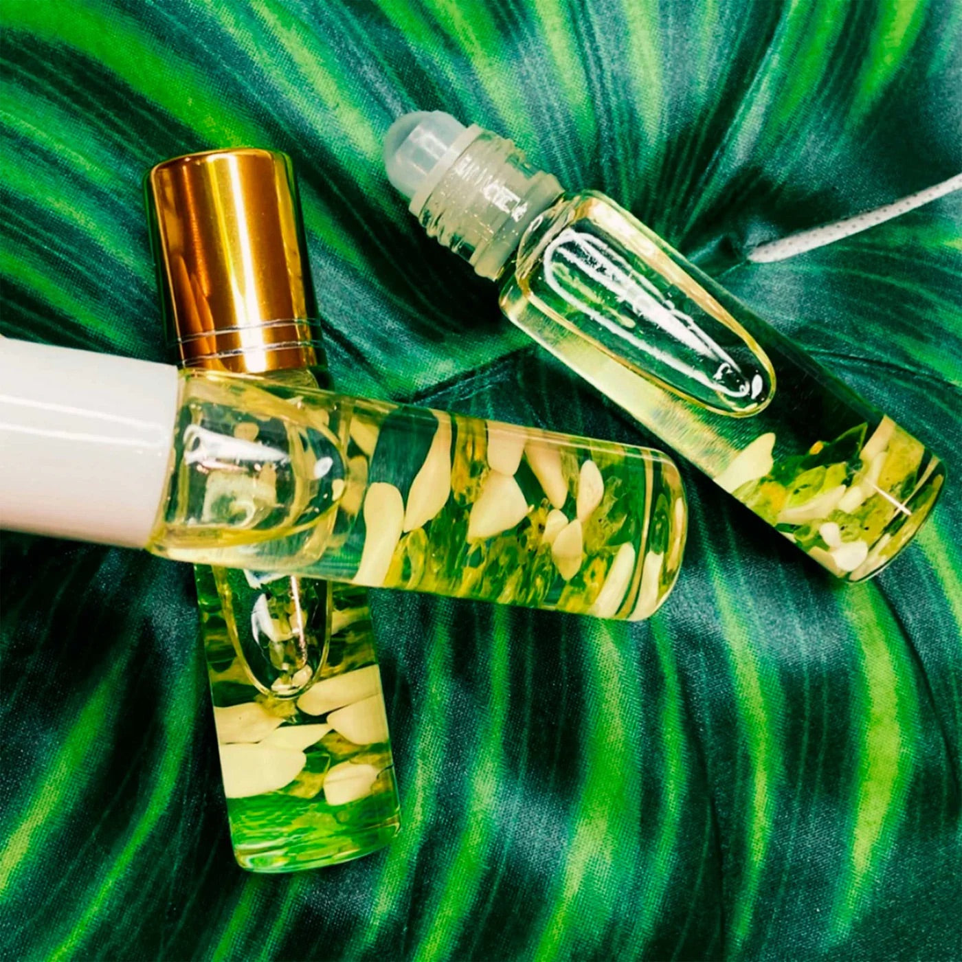 Close-up of three sandalwood kukui oil rollers against a variegated-leaf background.